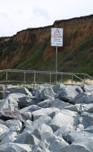 Dry stones, beneath crumbly cliffs with warning sign, Ruth's coastal walk.